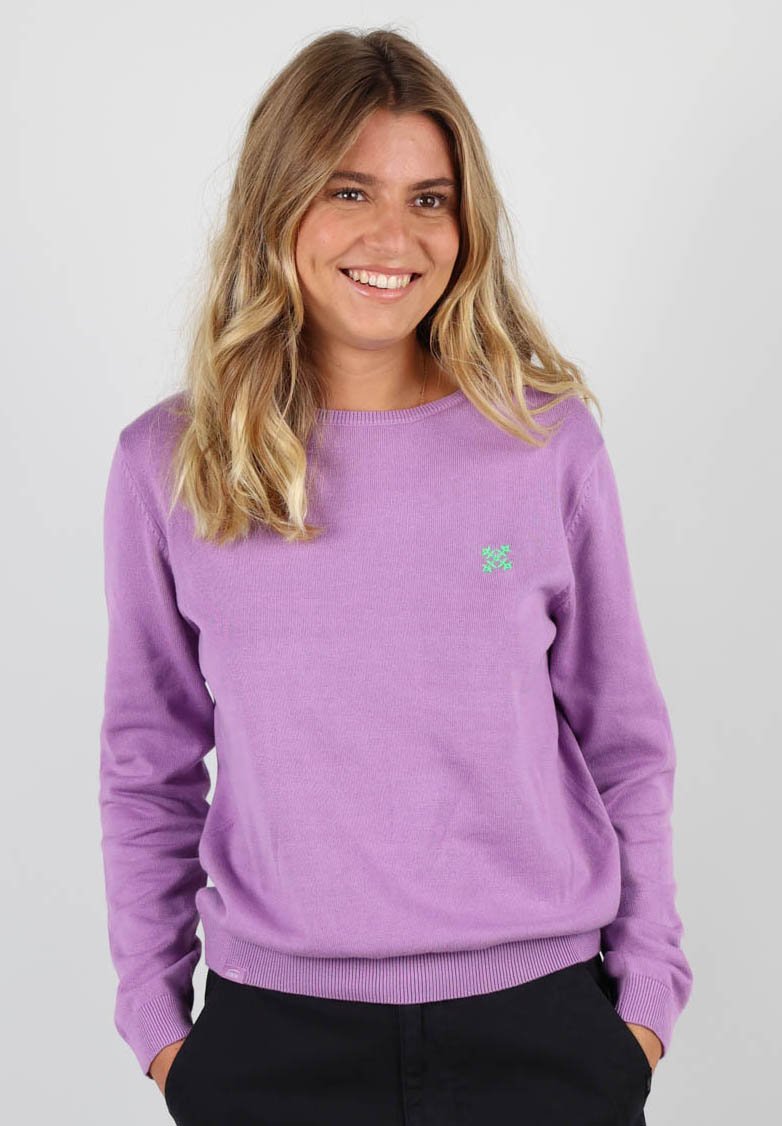 Pull léger en violet pâle avec un col rond, des poignets et un ourlet côtelés, arborant un petit logo vert sur la poitrine. Matière en tricot douce.