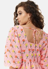 Pink floral dress featuring puffed sleeves, textured fabric, and a scoop back with a tying detail. Decorated with orange and yellow flowers.