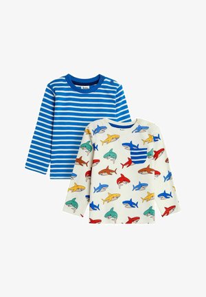 Dve srajce z dolgimi rokavi: ena z modrimi vodoravnimi črtami in druga smetana barve s pisanimi odtisi morskih psov ter žepom z modrimi črtami.