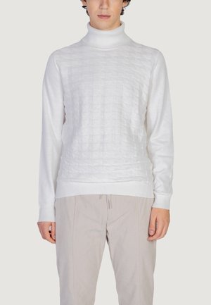 Maglione bianco a collo alto in maglia con motivo testurizzato sul davanti e polsini a costine. Abbinato a pantaloni in velluto a coste beige.