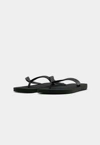 Une paire de sandales plates noires à lanières texturées, présentée sur un fond blanc uni.