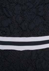 Černá květinová krajka s horizontálním bílým a černým proužkovaným elastickým páskem uprostřed.