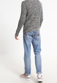 Grijze gebreide trui met een gestructureerd patroon, gecombineerd met lichtblauwe denim jeans. Bruin leren label op de jeans. Tan schoenen met witte zolen.