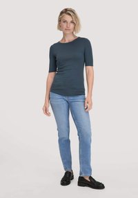 Donker teal pasvormige t-shirt met korte mouwen en lichtgewassen rechte jeans, gecombineerd met zwarte instappers, op een neutrale achtergrond.