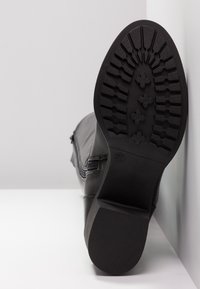 Botte en cuir noir positionnée debout montrant la semelle détaillée et la marque de taille 37 sur fond blanc.