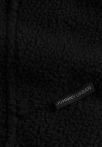 Tessuto in pile nero con una superficie morbida e texture e un'etichetta prominente con la scritta "JOHNNY URBAN" su uno sfondo nero.