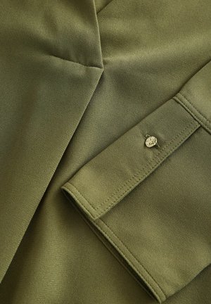 Olivově zelená látková košile s hladkou texturou. Obsahuje manžetu na knoflíky a přizpůsobené švy pro strukturovaný design.