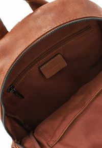 Wnętrze plecaka z brązowej skóry z kieszenią zapinaną na zamek, gładką fakturą i tkaninową podszewką; zawiera małą metkę marki.