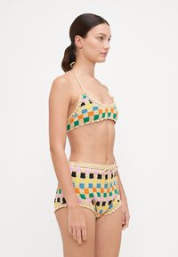 Bikini au crochet avec un motif en damier multicolore. Comprend des bretelles réglables, des bords festonnés et une taille à cordon sur le bas.