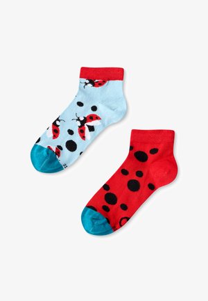 Calcetines tobilleros azules y rojos con patrones de mariquitas y lunares. El calcetín azul tiene un puño rojo y una base azul clara; el calcetín rojo presenta puntos negros.