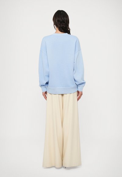 Φαρδιά φούτερ σε ανοιχτό γαλάζιο με χαμηλωμένους ώμους και ριμπ τελείωμα, συνδυασμένο με εκρού παντελόνι φαρδιάς γραμμής. Οπίσθια όψη, μινιμαλιστικό στυλ.