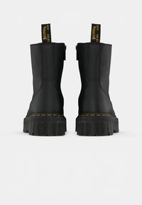 Black leather ankle boots with yellow stitching and contrasting pull tabs, featuring a chunky rubber sole and smooth texture.