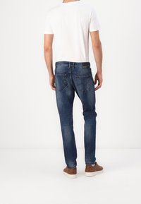 Jeans in denim slim fit di colore blu scuro con un leggero effetto vissuto, dotati di due tasche posteriori e una patch in pelle con logo sulla cintura.