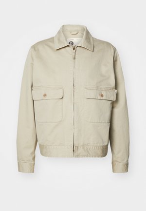 Light beige cotton jacket with a straight cut, zip closure, and two front patch pockets. Features a pointed collar and button accents.