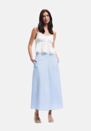 Witte top met kantafwerking en een aansluitend lijfje. Lange blauwe ruitjesrok met zakken. Model staat en draagt sandalen met bandjes.
