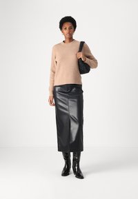 Beige gerippter Pullover, schwarze Leder-Midi-Rock und schwarze kniehohe Stiefel. Die gewebte schwarze Handtasche rundet das Outfit ab. Einfaches, modernes Design.