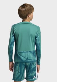 Green athletic shirt with long sleeves and a textured pattern, paired with matching shorts featuring white stripes on the sides.