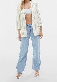 Bílý pruhovaný blejzr s třičtvrtečními rukávy, spárovaný s vysokým pasem lehkými modrými širokými džíny a sandály s průhledným podpatkem.