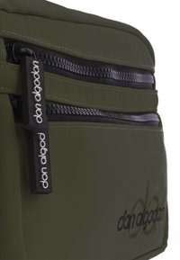 Bolsa de tela verde oliva con doble bolsillo con cremallera, presenta herrajes negros, textura suave y detalles de logo en bordado negro.