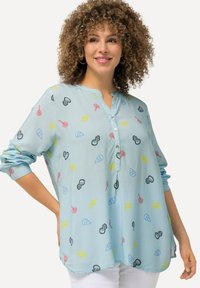 Camicia azzurra chiara, con bottoni e vestibilità rilassata. Presenta motivi colorati a tema caramelle e maniche lunghe arrotolate. Tessuto morbido al tatto.