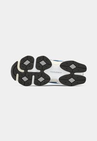 Sole of a New Balance sneaker showing black tread with diamond shapes on a white base against a plain background.