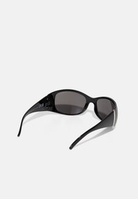 Schwarze Sonnenbrille mit einem eleganten, geschwungenen Design und dunklen Gläsern. Auffällige Metallakzente an den Gestellen, polierte Oberfläche und glatte Textur.