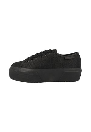 Zapatilla negra con plataforma, parte superior de tela texturizada, cierre de cordones y suela gruesa de goma, mostrada de lado sobre fondo blanco.