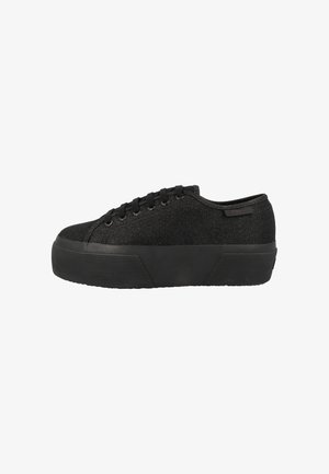 Zapatilla negra con plataforma, parte superior de tela texturizada, cierre de cordones y suela gruesa de goma, mostrada de lado sobre fondo blanco.