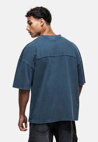 Chemise à manches courtes surdimensionnée en bleu foncé, fabriquée en coton doux. Dispose d'un ourlet brut et d'un design en panneaux dans le dos.