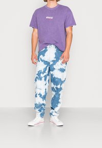 Lila bomulls-t-shirt med texten "MOUNT FUJI". Blå denimjeans med vitt molnmönster. Vita sneakers. En enkel, avslappnad outfit.