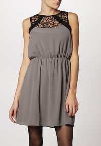 Ärmeloses graues Kleid mit schwarzer Spitze am Ausschnitt. Mit einem elastischen Bund und fließendem Stoff für eine lässige Passform.