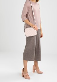 Borsa a tracolla trapuntata rosa chiaro con forma rettangolare, caratterizzata da un bordo a contrasto e una tracolla regolabile, indossata con pantaloni larghi grigi.