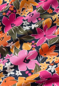 Tissu floral avec de grandes fleurs roses, orange et blanches sur un fond bleu marine foncé, avec des feuilles vertes et de petits accents colorés.