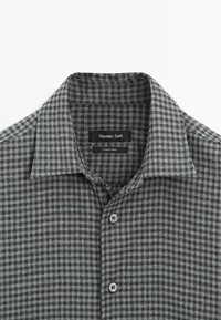 Grå- och svartmönstrad skjorta med knappkrage, med en etikett som visar "Massimo Dutti" och två grå knappar framtill.