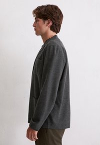 Grijze wollen blazer met een mandarijnkraag, zijzakken en een ontspannen pasvorm, zijaanzicht tegen een lichte achtergrond.