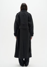 Manteau noir en tissu léger, avec une taille ceinturée, un col cranté et des manches longues. La vue arrière montre une coupe droite.