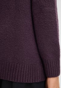 Maglione viola con texture, dotato di polsini e orlo a coste. Il tessuto appare morbido e peloso, con una vestibilità leggermente ampia.