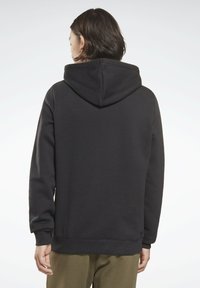 Sudadera negra hecha de tela suave con un corte relajado, que presenta una gran capucha y puños acanalados, vista desde la parte de atrás.