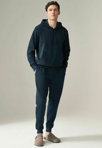 Sudadera de un oscuro azul marino con un bolsillo frontal y cordones, combinada con pantalones de cintura elástica, ambos de tela suave. Los pantalones tienen puños ajustados.