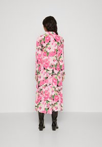 Floral midi dress featuring a pink and green pattern, long sleeves, a collared neck, and a flowy silhouette. Worn with black knee-high boots.