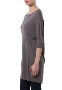 Grå oversized tunika med trekvartsärmar, sidfickor och lös passform; tyget verkar mjukt och faller lätt.