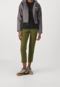 Szara krótka kurtka, czarny t-shirt, oliwkowe spodnie do kostek oraz wielokolorowe buty trekkingowe z fakturowaną podeszwą.