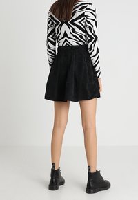 Zwarte ribstoffen rok met plooien, gecombineerd met een zwart-wit gestreepte top met lange mouwen. De schoeisel bestaat uit zwarte enkellaarsjes.