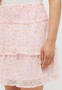 Jupe florale rose avec taille froncée, présentant un design à plusieurs couches et un tissu doux et transparent orné de motifs floraux jaunes et roses dispersés.