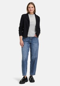 Černý kardigan s roztrhanými okraji přes pruhované tričko, zkombinovaný se světle modrými džíny a černými platformovými mokasíny. Hladká textura, uvolněný střih.