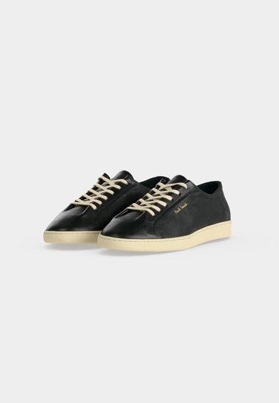 Paire de baskets en cuir noir avec des lacets et semelles blanches, avec un petit texte de logo doré sur le côté, sur fond blanc.