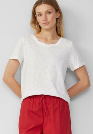 T-shirt blanc à manches courtes avec un col rond et une texture subtile, associé à un pantalon rouge ample avec une taille élastique et un cordon de serrage.