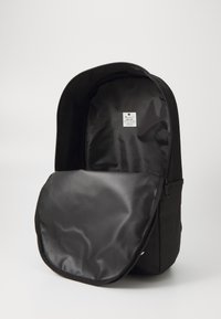 Schwarzer Rucksack mit einer glatten Nylonaußenfläche, geräumigem Hauptfach, vorderer Reißverschlusstasche und einem Etikett im Inneren.