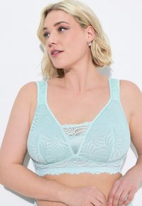 Bralette in pizzo verde menta chiaro, con motivi floreali, bordi ondulati e una scollatura profonda con una fascia larga sotto il seno e spalline regolabili.