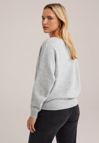 Pulover oversized de culoare gri deschis, dintr-un material moale și tricotat. Are un tiv ribatat și mâneci largi, cu o croială lejeră. Blugii negri completează ținuta.